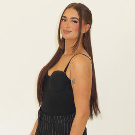 Woman wearing a black top and striped pants against a plain background