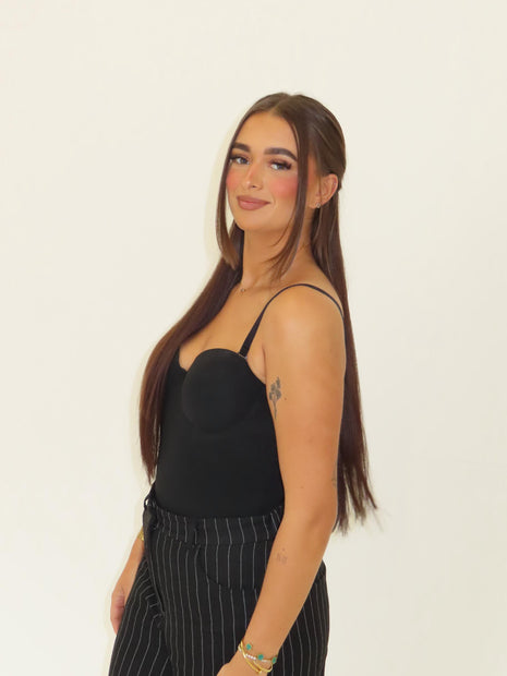 Woman wearing a black top and striped pants against a plain background