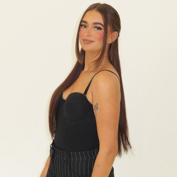 Woman wearing a black top and striped pants against a plain background