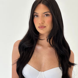 Woman with long black hair wearing a white top on a plain background