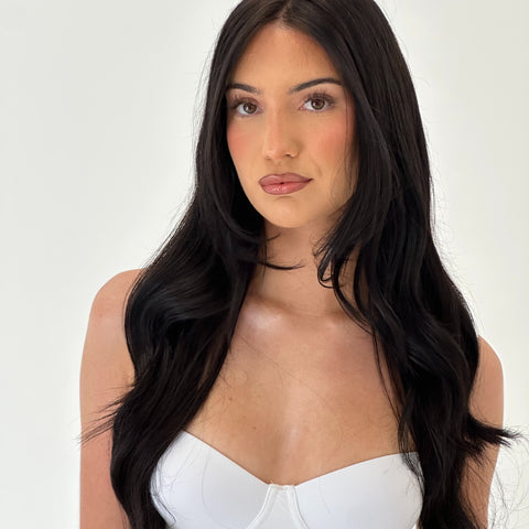 Woman with long black hair wearing a white top on a plain background