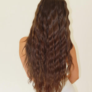 Person with long, wavy brown hair on a plain background