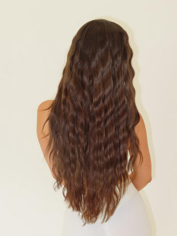 Person with long, wavy brown hair on a plain background